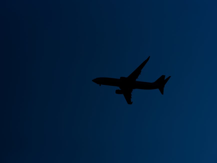 Silhouette of an airplane flying against a blue evening sky, showcasing graceful flight.